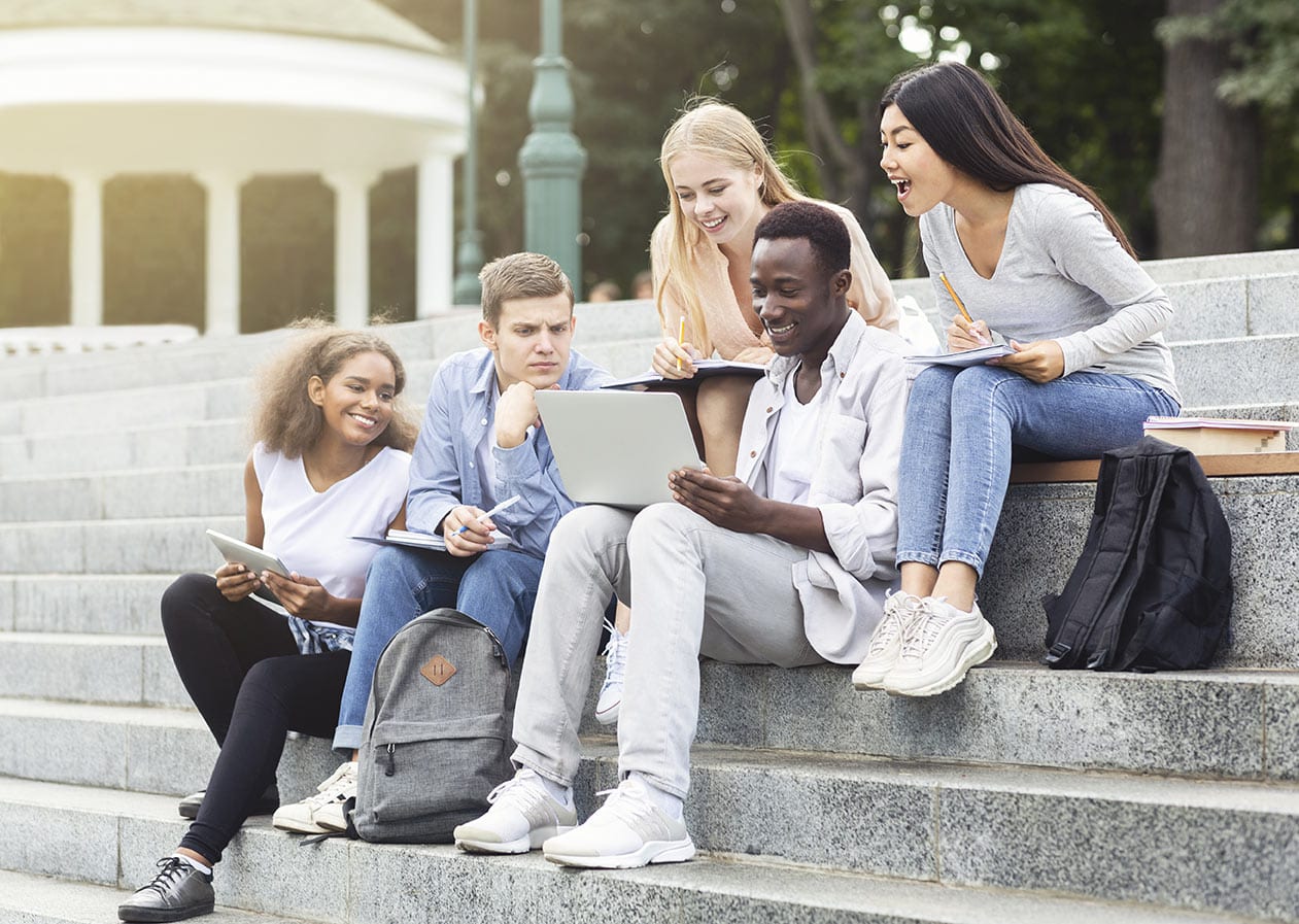 Gruppe junger, diverser Menschen schaut gemeinsam in einen Laptop
